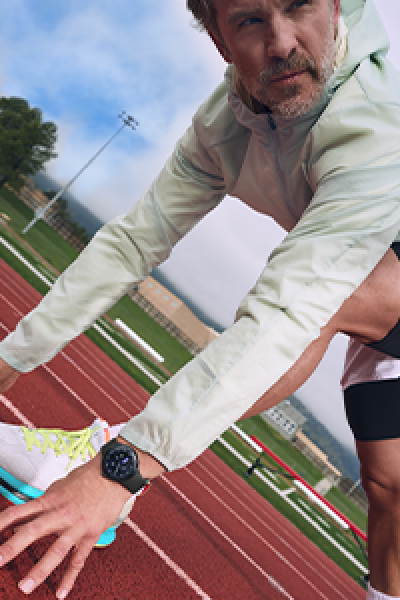 Man in white athletic jacket wearing a Google Pixel Watch on a red running track