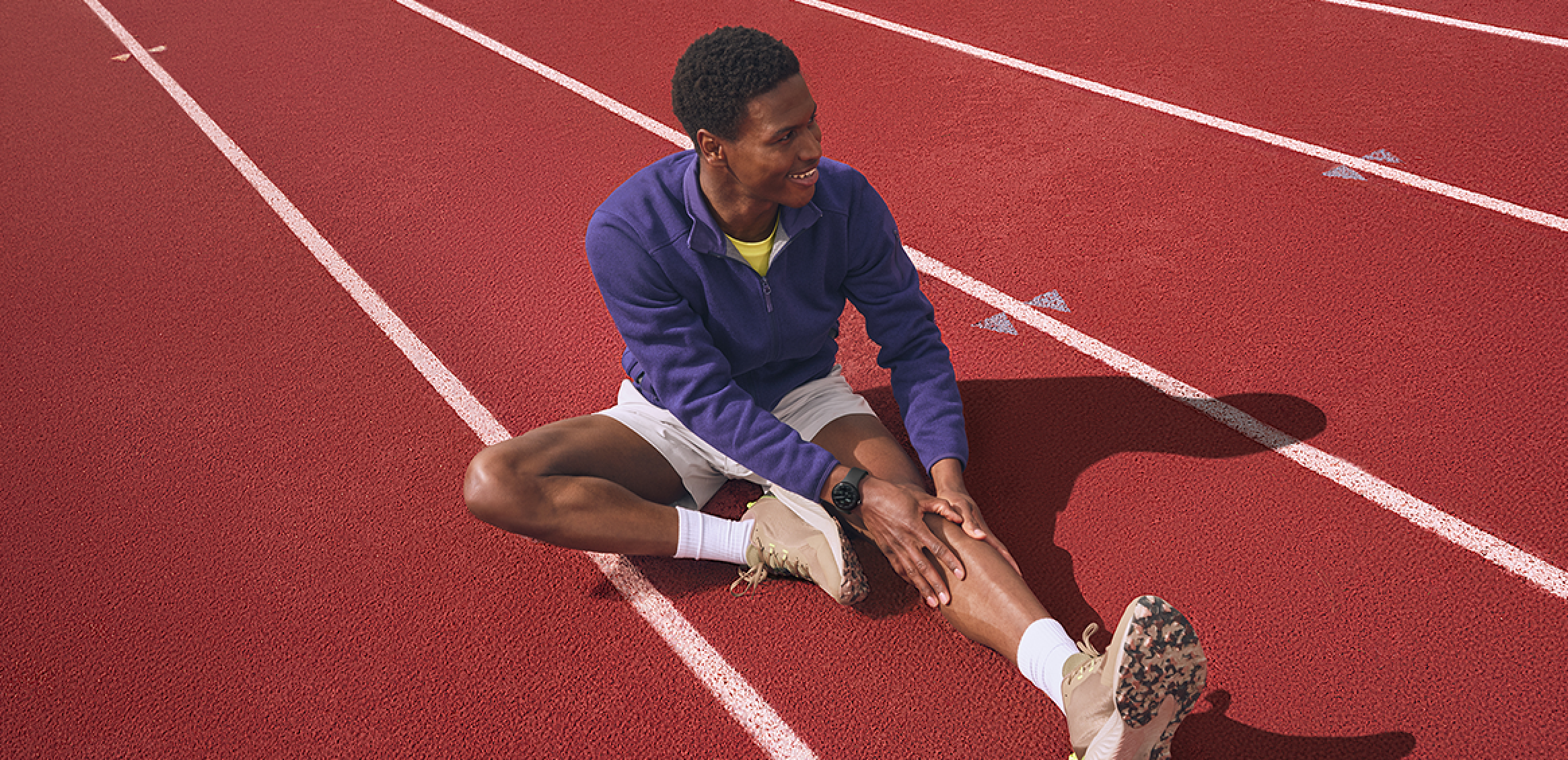 Runner stretching on red track wearing the Google Pixel Watch and blue athletic wear